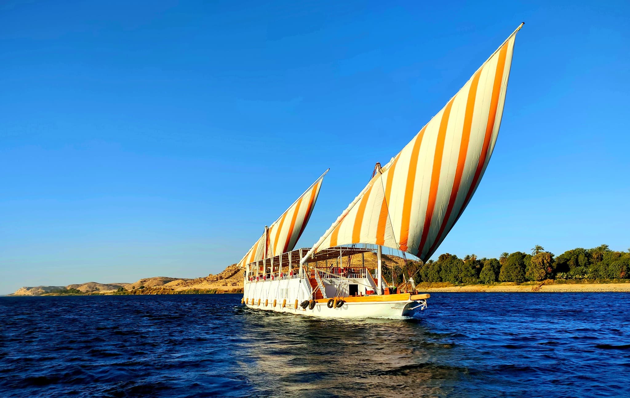 Dahabiya en navigation sur le Nil avec ses voiles rayées orange et blanc, Rendez-vous sur le Nil